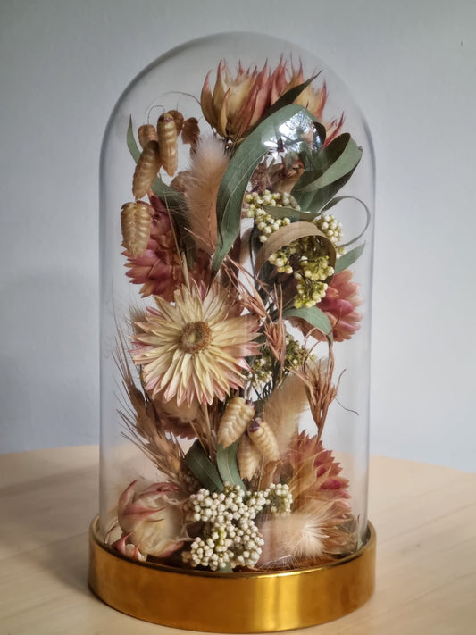 19cm glass dome with golden base featuring native Australian flowers and wild grases  in greens, blush and dusty rose.