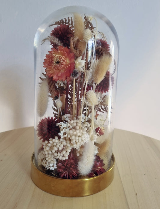 19cm glass dome with golden base features an abundance of dried wildflowers and foliages in deep reds, browns and ivory. 